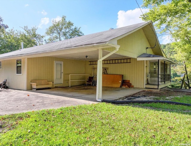 back of property with driveway, an attached carport, and a yard