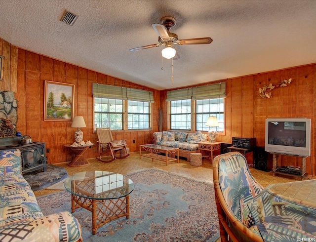 living area with wood walls, vaulted ceiling, a wood stove, a ceiling fan, and visible vents