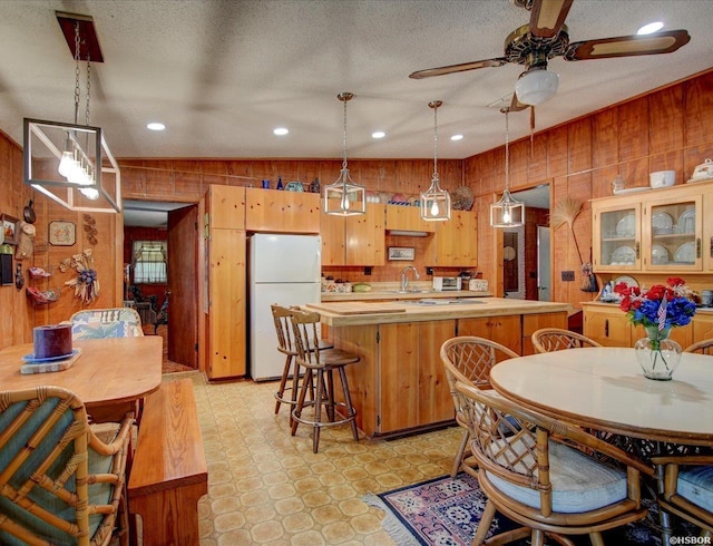 kitchen with a ceiling fan, wooden walls, light floors, light countertops, and freestanding refrigerator