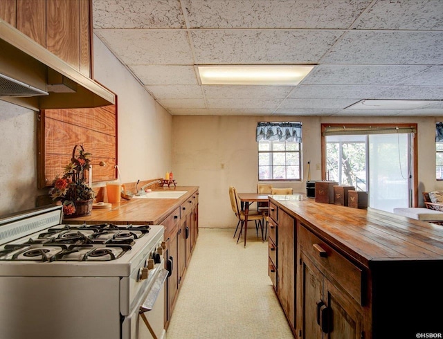 kitchen with a paneled ceiling, white gas range oven, wooden counters, and a sink