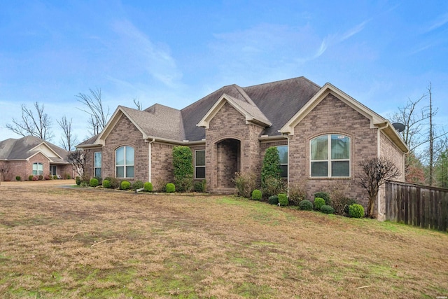 view of front facade with a shingled roof, fence, a front lawn, and brick siding