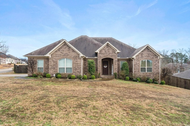 ranch-style house with brick siding, a front lawn, a shingled roof, and fence