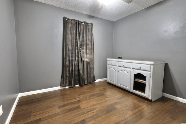 unfurnished room with ceiling fan, a textured ceiling, baseboards, and dark wood-type flooring