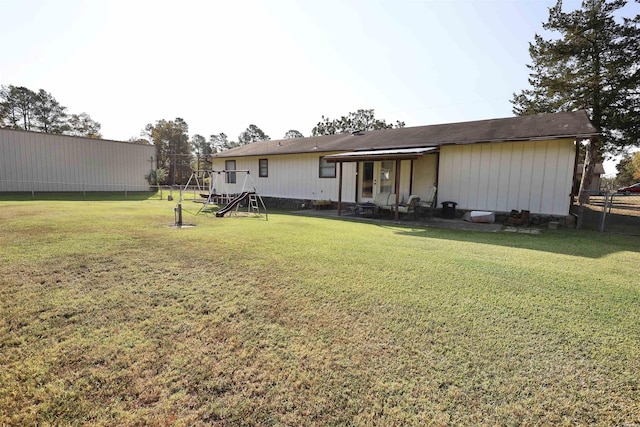 back of property featuring a lawn, a playground, and fence