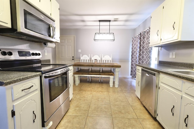 kitchen with dark countertops, white cabinetry, stainless steel appliances, and hanging light fixtures