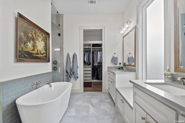 full bath featuring a freestanding bath, two vanities, a sink, and tile walls