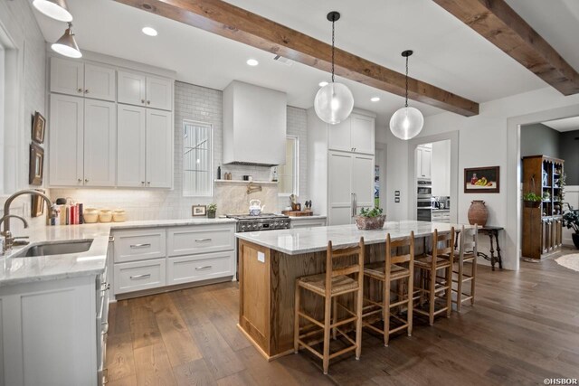 kitchen featuring a kitchen island, light stone counters, wall chimney range hood, white cabinetry, and a sink