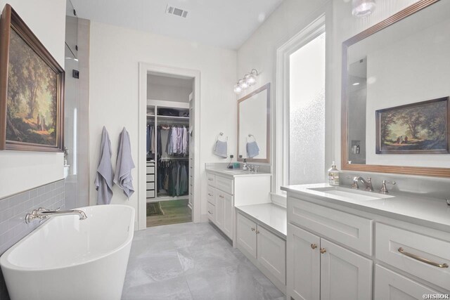 full bath with marble finish floor, visible vents, a spacious closet, vanity, and a freestanding tub