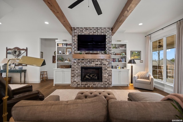 living area featuring light wood-style flooring, a fireplace, ceiling fan, and beamed ceiling