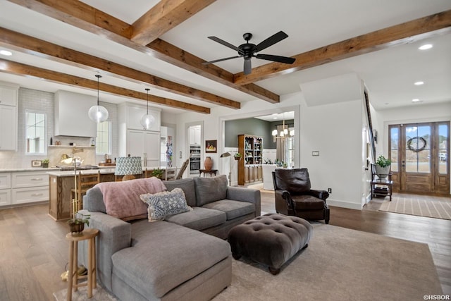 living area with light wood-style flooring, ceiling fan with notable chandelier, beam ceiling, and recessed lighting