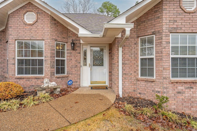 view of exterior entry featuring brick siding and roof with shingles