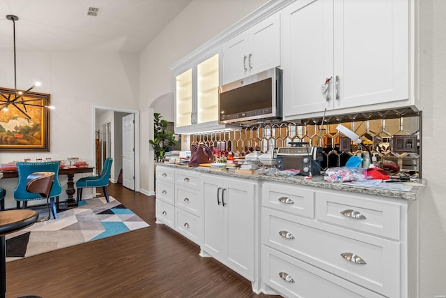 kitchen with white cabinets, dark wood-style floors, stainless steel microwave, light stone counters, and hanging light fixtures