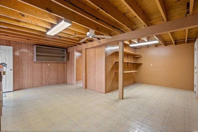 finished below grade area featuring light floors, a ceiling fan, and wood walls