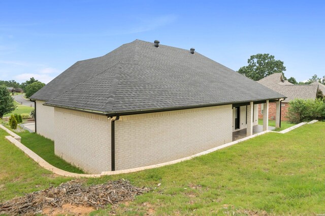 rear view of house featuring a shingled roof, a lawn, and brick siding