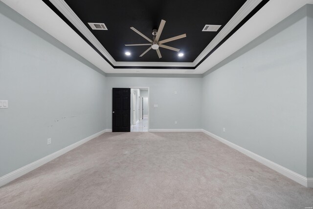 spare room featuring light colored carpet, visible vents, baseboards, a raised ceiling, and crown molding