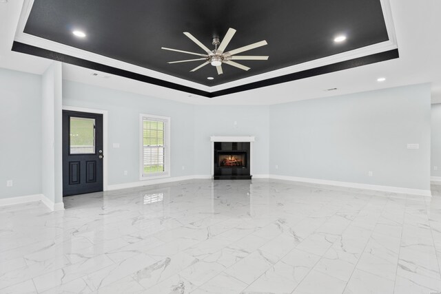 unfurnished living room featuring a warm lit fireplace, ceiling fan, baseboards, marble finish floor, and a raised ceiling