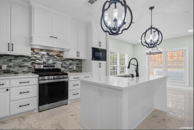 kitchen featuring black microwave, marble finish floor, light countertops, an island with sink, and gas stove