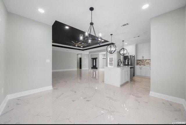 kitchen featuring open floor plan, a kitchen island with sink, light countertops, white cabinetry, and pendant lighting