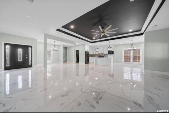 unfurnished living room featuring a tray ceiling, marble finish floor, baseboards, and ceiling fan with notable chandelier