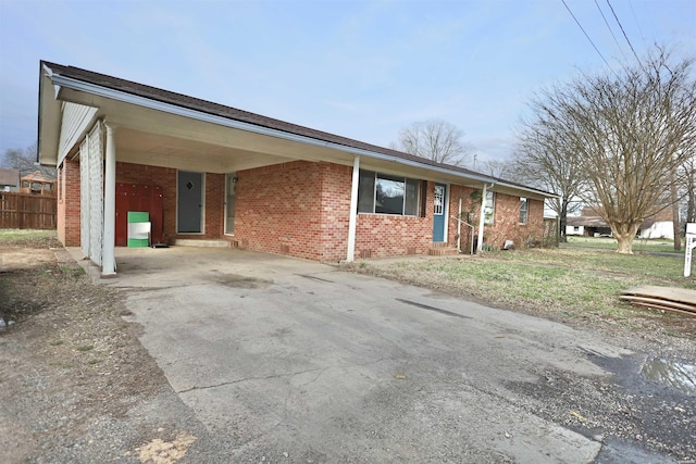 ranch-style house featuring an attached carport, brick siding, driveway, and fence