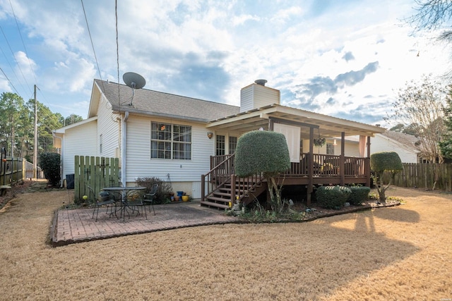 back of house with a deck, a patio, fence, roof with shingles, and a chimney