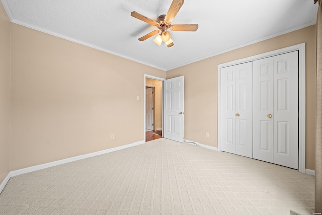 unfurnished bedroom featuring light carpet, a ceiling fan, baseboards, a closet, and crown molding