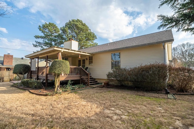 back of house featuring a shingled roof, a yard, a chimney, and a wooden deck