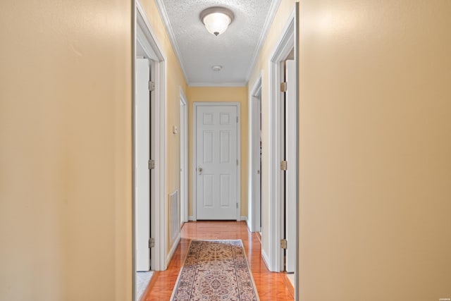 hallway with light wood-type flooring, visible vents, a textured ceiling, and baseboards