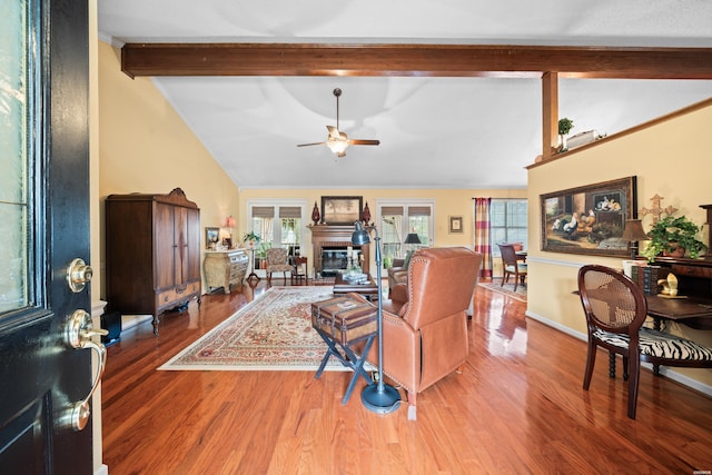 living room with a ceiling fan, a glass covered fireplace, vaulted ceiling with beams, and wood finished floors