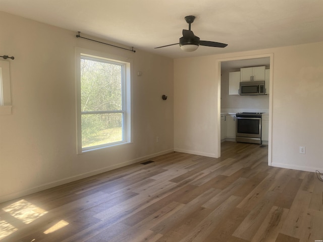 spare room with light wood-type flooring, visible vents, baseboards, and a ceiling fan