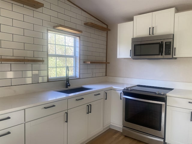 kitchen featuring stainless steel appliances, a sink, white cabinetry, vaulted ceiling, and light countertops