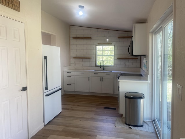 kitchen featuring lofted ceiling, freestanding refrigerator, light countertops, light wood-style floors, and a sink