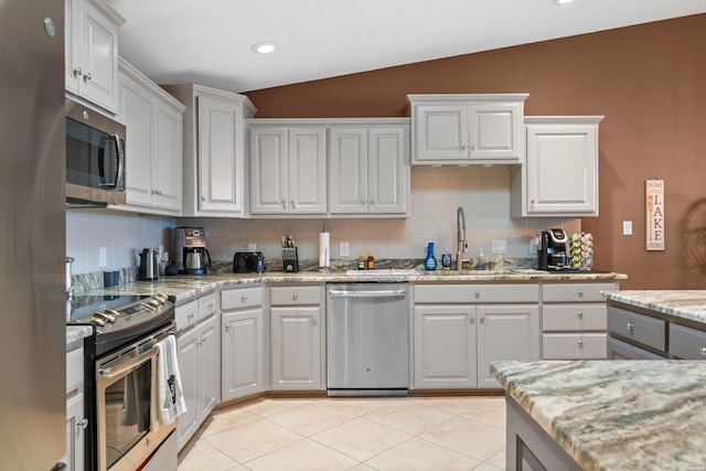 kitchen with a sink, backsplash, stainless steel appliances, light tile patterned flooring, and vaulted ceiling