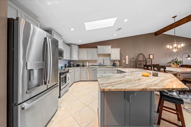 kitchen with a breakfast bar, stainless steel appliances, vaulted ceiling with skylight, light tile patterned floors, and hanging light fixtures