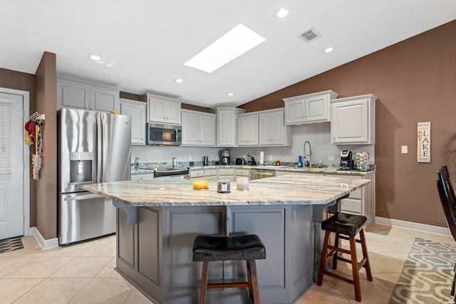 kitchen with light tile patterned floors, light stone countertops, visible vents, appliances with stainless steel finishes, and a center island