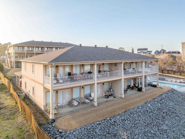 back of house with fence, a shingled roof, an outdoor pool, a balcony, and a patio area