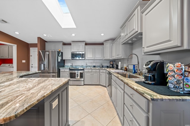 kitchen with gray cabinetry, a sink, backsplash, appliances with stainless steel finishes, and light tile patterned floors