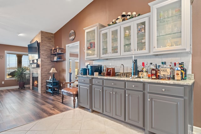 bar with light tile patterned flooring, a sink, decorative backsplash, vaulted ceiling, and a large fireplace