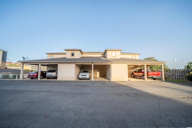 view of front facade featuring stucco siding, covered parking, and fence