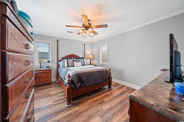 bedroom featuring wood finished floors, visible vents, baseboards, a textured ceiling, and crown molding