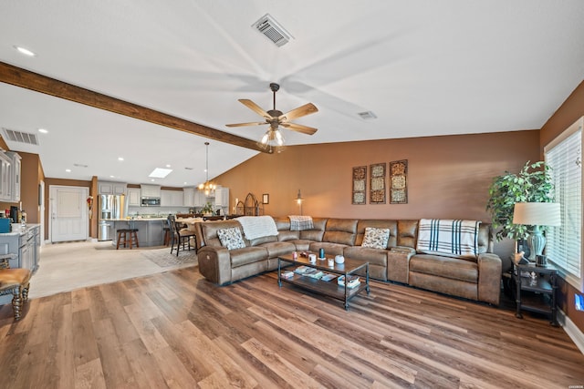 living room with lofted ceiling with beams, light wood-style flooring, ceiling fan with notable chandelier, and visible vents