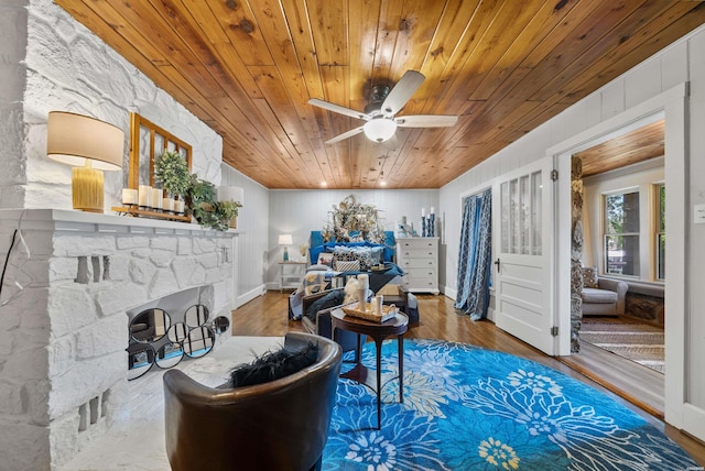 sitting room with a ceiling fan, wood ceiling, a stone fireplace, and wood finished floors