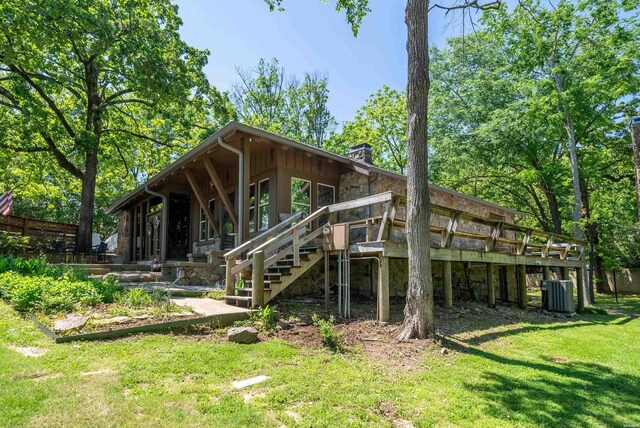 back of property with a chimney, a lawn, stairway, cooling unit, and stone siding