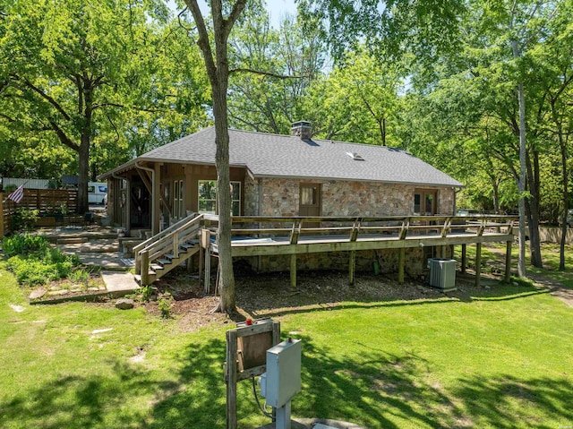 back of house featuring stone siding, a shingled roof, and a lawn