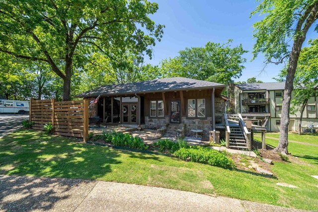 rear view of property with stairs, stone siding, and a yard