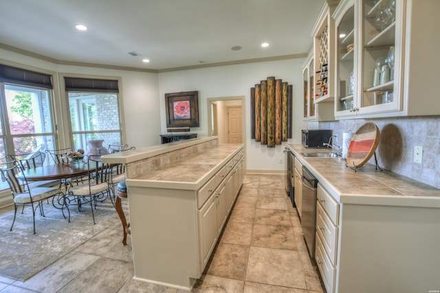 kitchen featuring tasteful backsplash, dishwasher, tile countertops, glass insert cabinets, and a kitchen breakfast bar