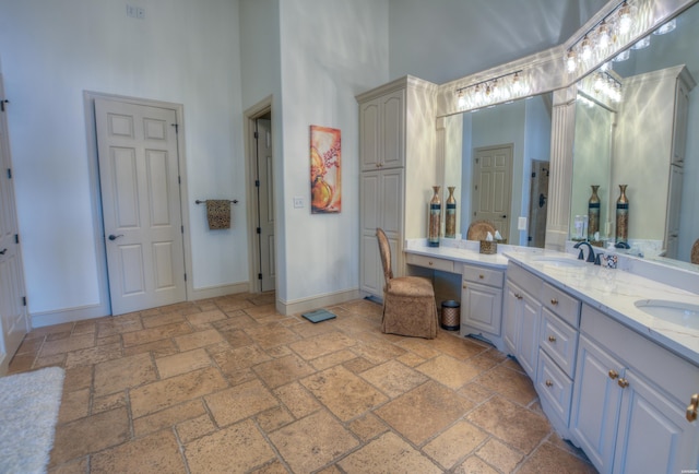 bathroom with stone tile floors, double vanity, a towering ceiling, a sink, and baseboards