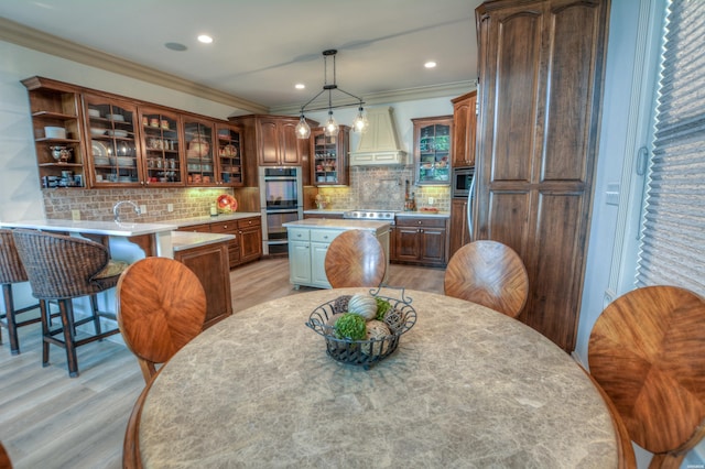 kitchen with a kitchen island, glass insert cabinets, appliances with stainless steel finishes, custom exhaust hood, and light countertops