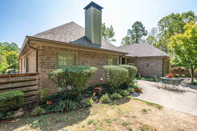 back of property with brick siding, roof with shingles, fence, and a patio