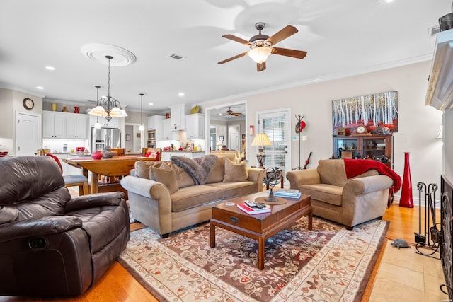 living room with ornamental molding, visible vents, and ceiling fan with notable chandelier